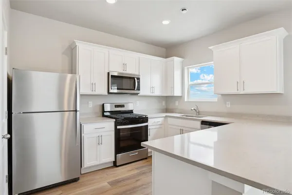 a kitchen with stainless steel appliances granite countertop white cabinets a sink dishwasher and a stove with wooden floor