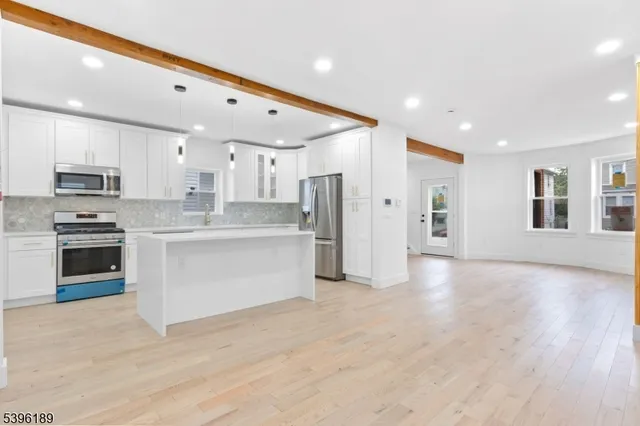 a large white kitchen with stainless steel appliances granite countertop a stove a sink a refrigerator and white cabinets with wooden floor