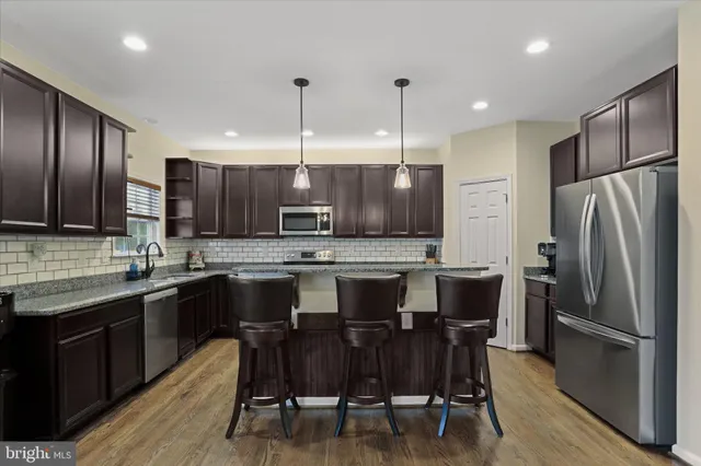 a kitchen with stainless steel appliances a sink a stove a refrigerator cabinets and wooden floor