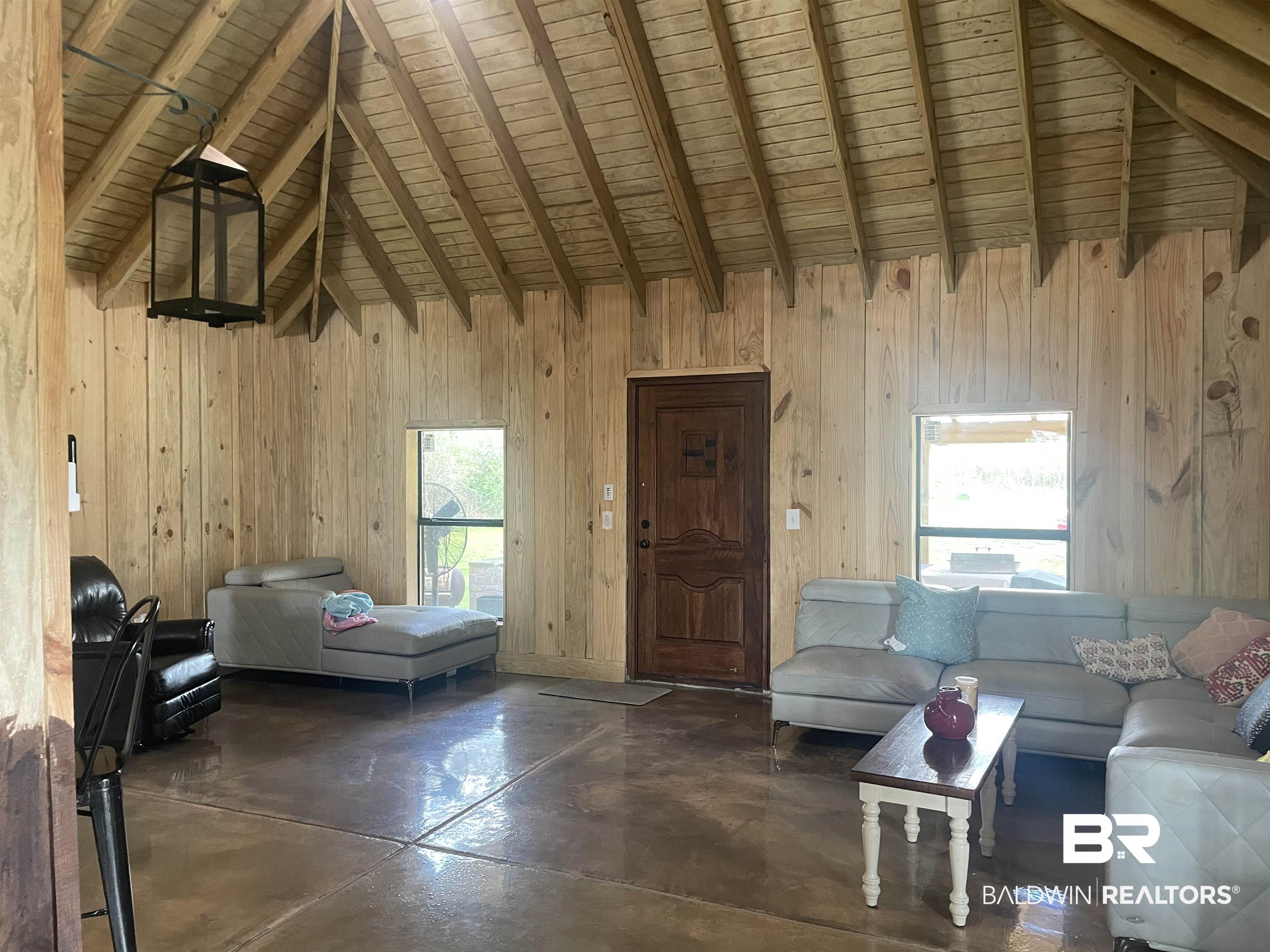 21593 Hubbard Road Robertsdale, AL 36567 - Photo 16 of 22 Unfurnished living room featuring beam ceiling, wooden walls, finished concrete floors, and high vaulted ceiling