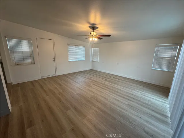 an empty room with wooden floor chandelier fan and windows