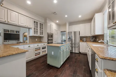 a kitchen with stainless steel appliances granite countertop a stove top oven a sink dishwasher and a refrigerator with wooden floor