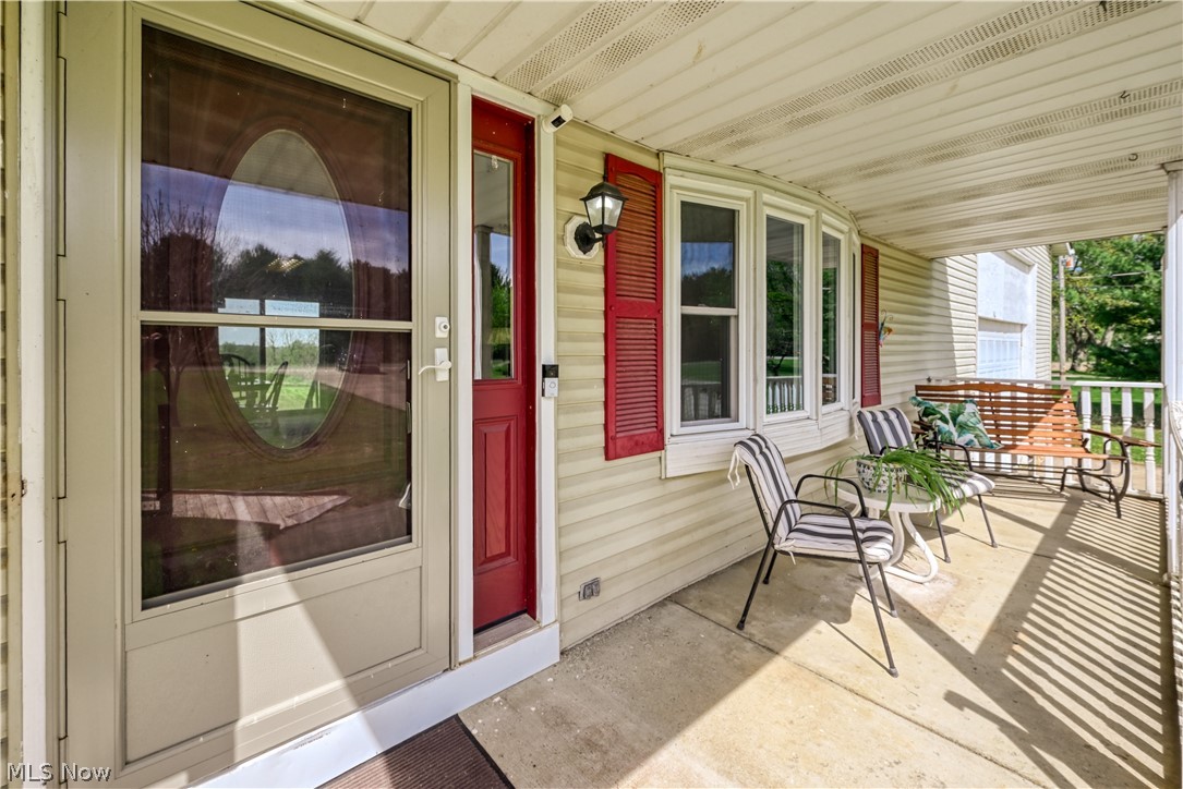 4715 Rock Spring Road Ravenna, OH 44266 - Photo 20 of 21 Covered front porch featuring a red entry door with sidelight, bay windows with louvered shutters, and vinyl siding