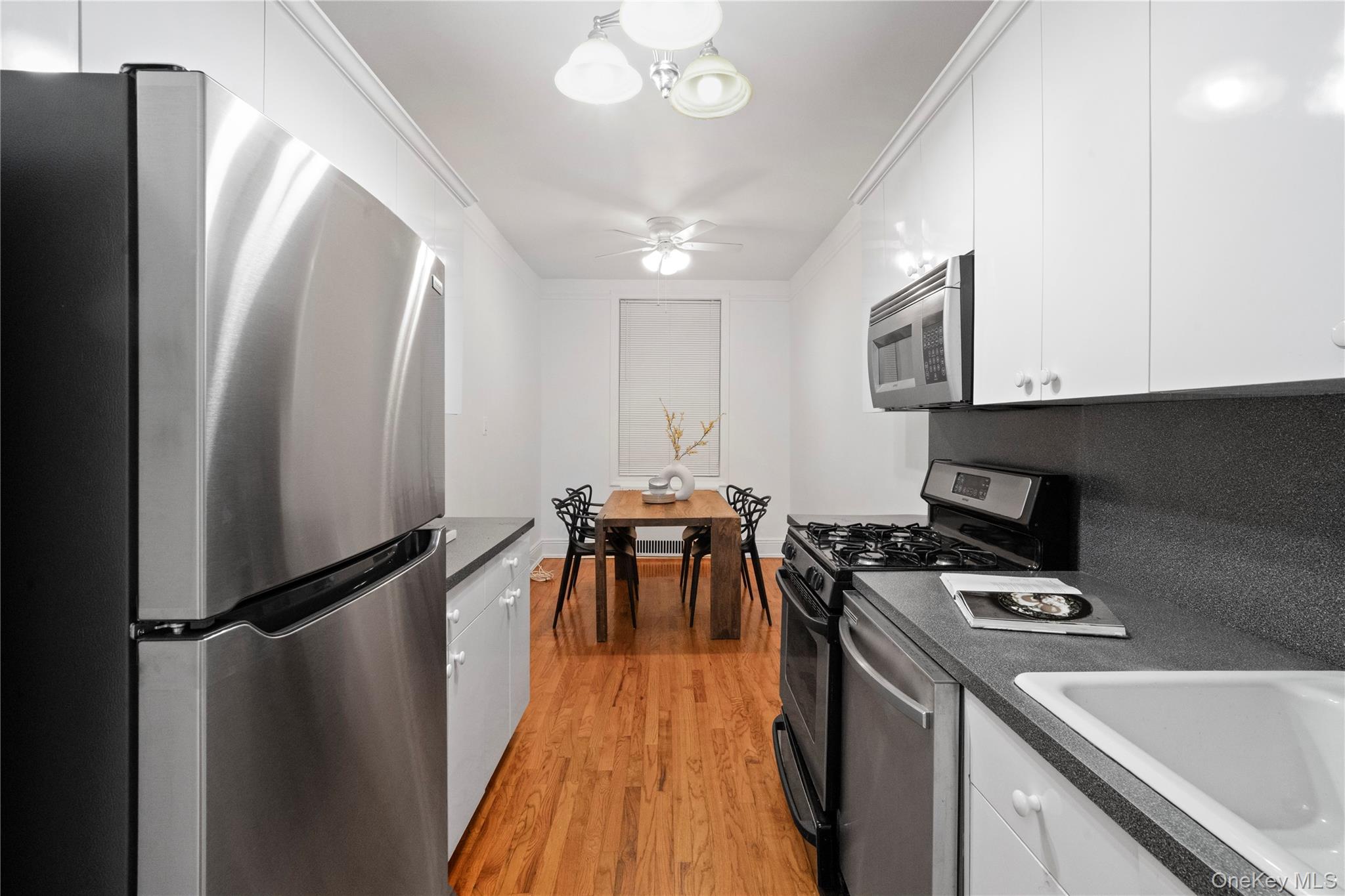 110-21 73rd Road, Unit 5H Queens, NY 11375 - Photo 5 of 14 a kitchen with stainless steel appliances granite countertop a refrigerator a sink dishwasher a stove and a dining table with wooden floor
