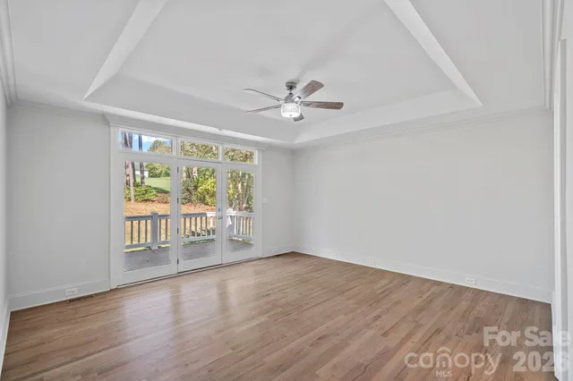 a view of an empty room with wooden floor and a ceiling fan