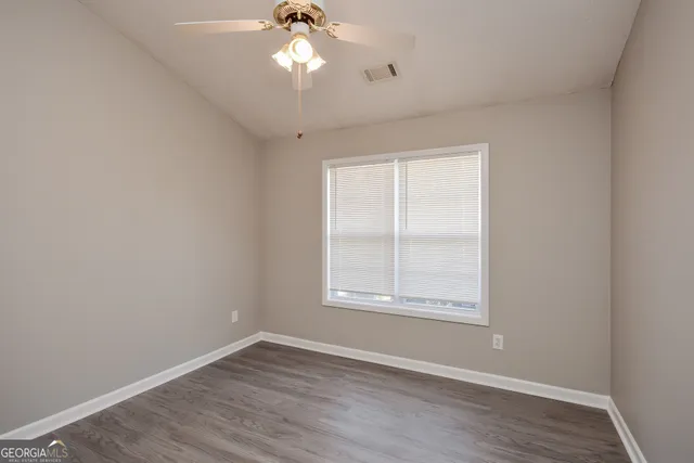an empty room with wooden floor fan and windows