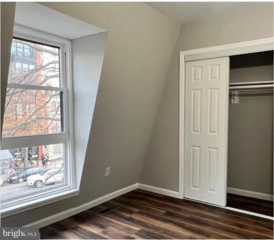 an empty room with wooden floor closet and windows