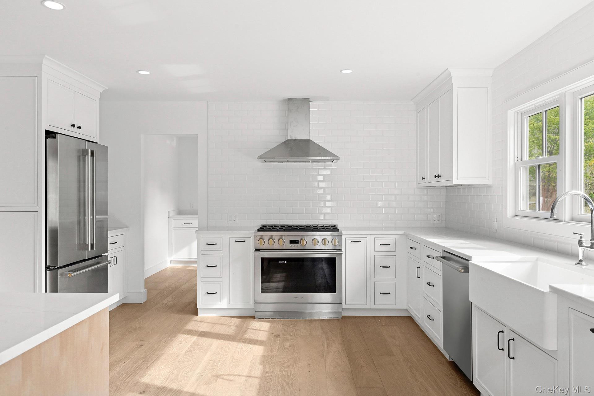 5 Pheasant Lane Remsenburg, NY 11960 - Photo 7 of 27 Kitchen with stainless steel appliances, tasteful backsplash, light wood-type flooring, white cabinets, and wall chimney exhaust hood