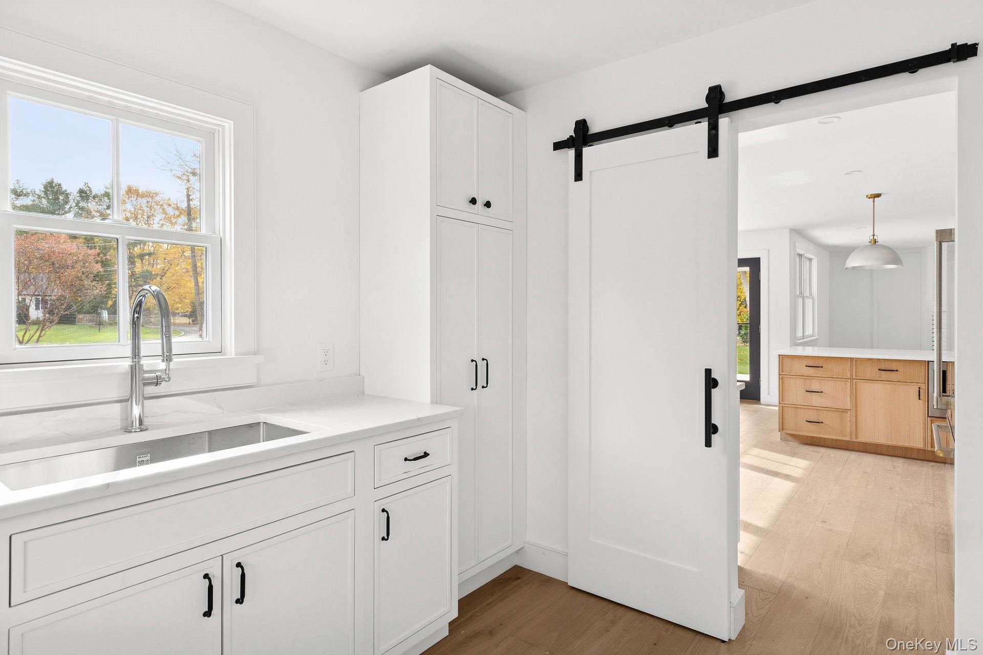 5 Pheasant Lane Remsenburg, NY 11960 - Photo 8 of 27 Kitchen featuring a barn door, light wood-type flooring, hanging light fixtures, and white cabinetry