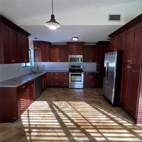 a kitchen with stainless steel appliances granite countertop a refrigerator a stove and a sink with wooden cabinets