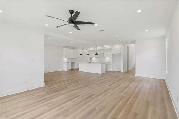 a view of an empty room with wooden floor and a ceiling fan