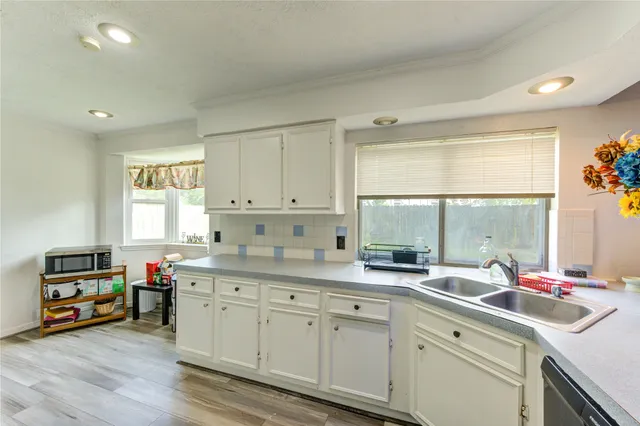 a kitchen with kitchen island granite countertop a sink dishwasher stove and white cabinets with wooden floor