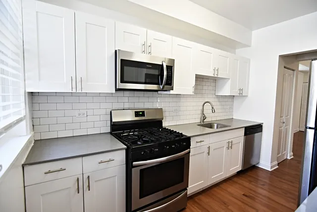 a kitchen with stainless steel appliances granite countertop white cabinets a sink a stove a microwave and cabinetry