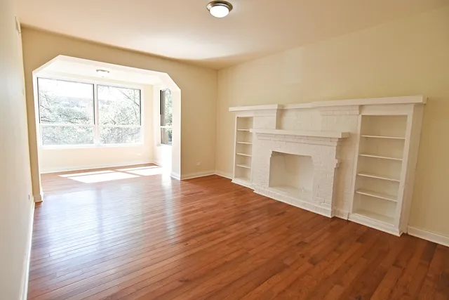an empty room with wooden floor cabinet and windows