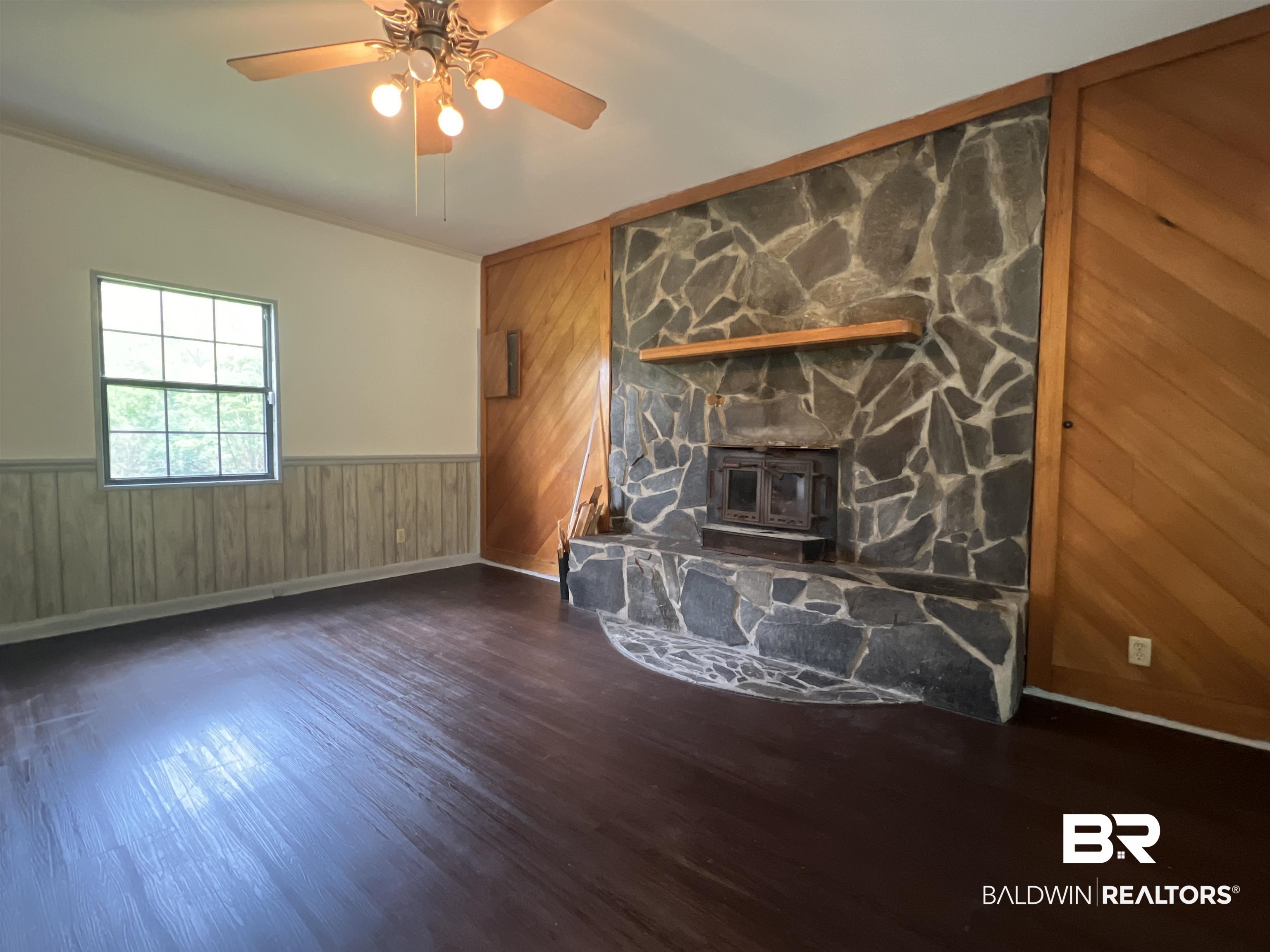 13301 A Hugh Fort Road Grand Bay, AL 36541 - Photo 17 of 34 Unfurnished living room featuring wooden walls, a wood stove, wood finished floors, a ceiling fan, and crown molding