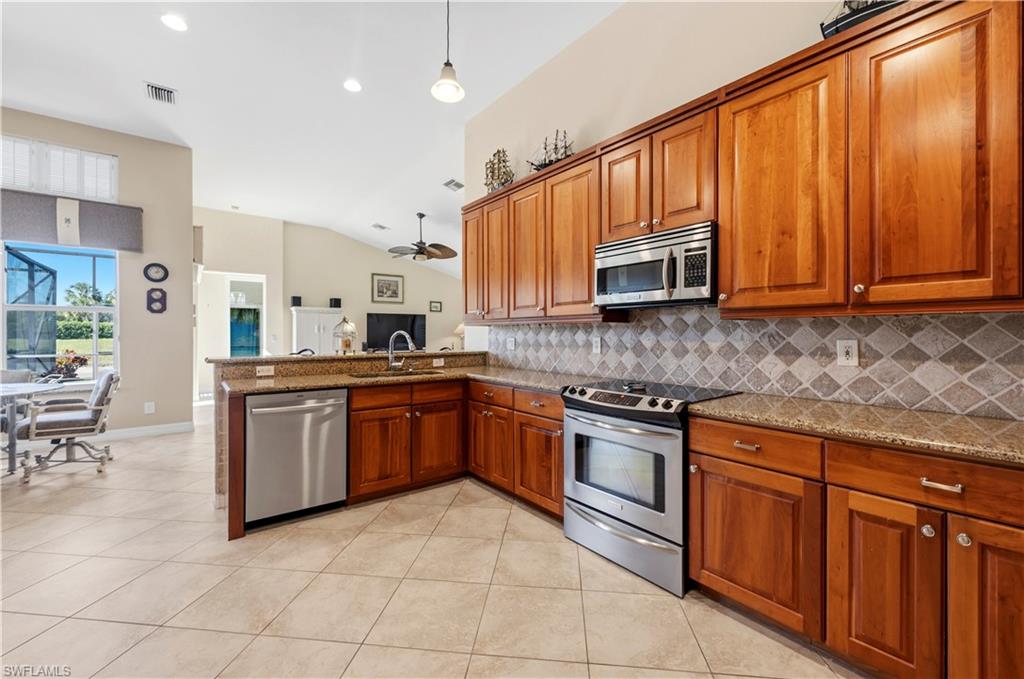 1411 Princess Sabal Point Naples, FL 34119 - Photo 8 of 32 Kitchen featuring wood finish cabinets, stainless steel appliances, dark stone counters, light tile patterned floors, and vaulted ceiling