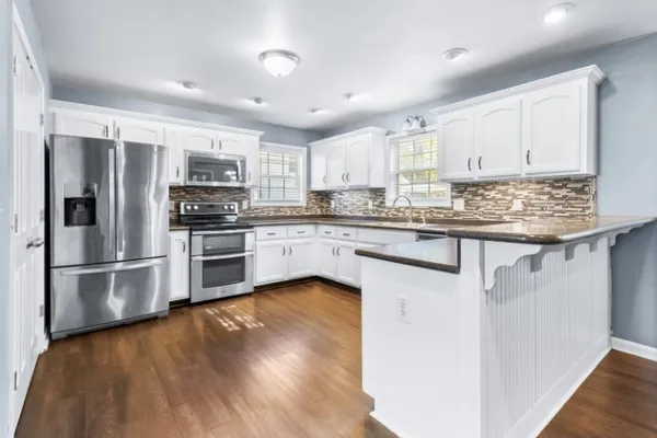 a kitchen with stainless steel appliances granite countertop a stove top oven a refrigerator a sink and dishwasher with wooden floor
