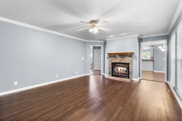 an empty room with wooden floor a ceiling fan a fireplace and windows