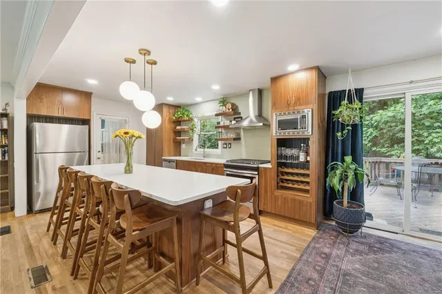 a kitchen with stainless steel appliances kitchen island granite countertop a refrigerator a oven a sink and a dining table with wooden floor