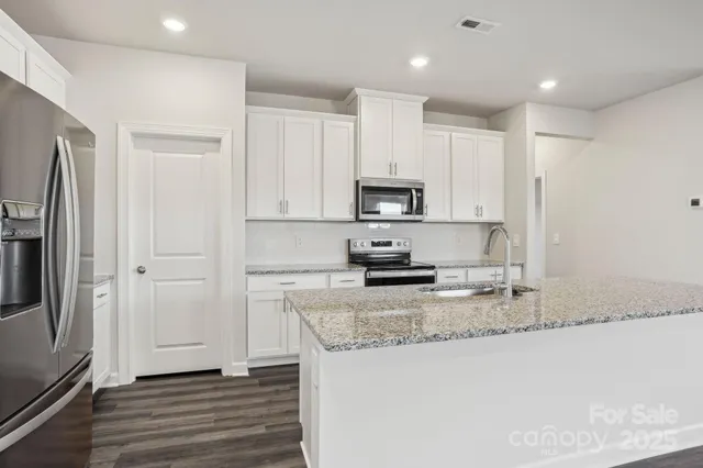 a kitchen with stainless steel appliances granite countertop a refrigerator a stove a sink and white cabinets