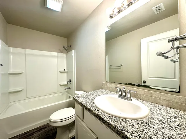 a bathroom with a granite countertop sink toilet mirror and bathtub