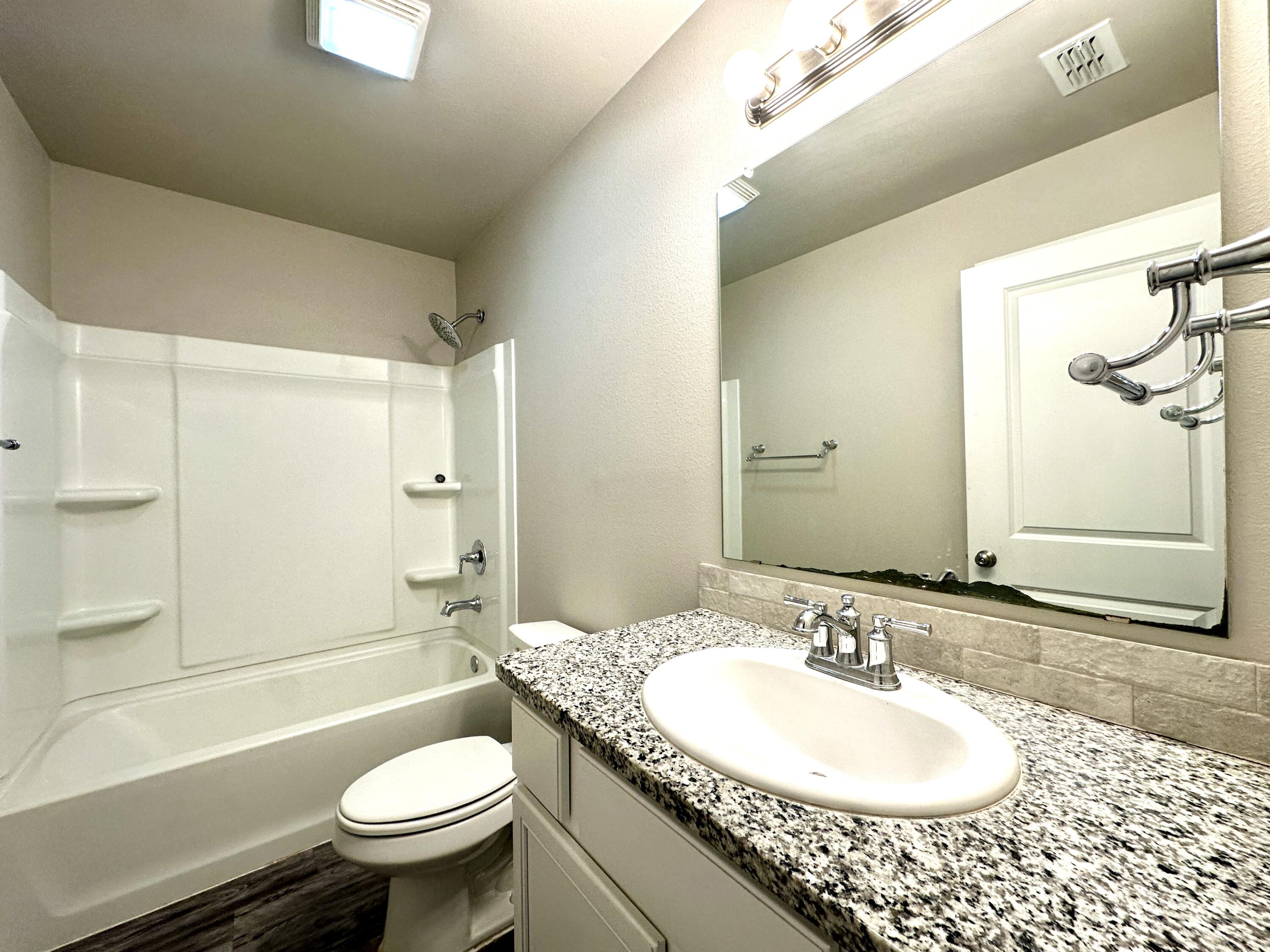 7526 31st Place Lubbock, TX 79407 - Photo 13 of 14 a bathroom with a granite countertop sink toilet mirror and bathtub
