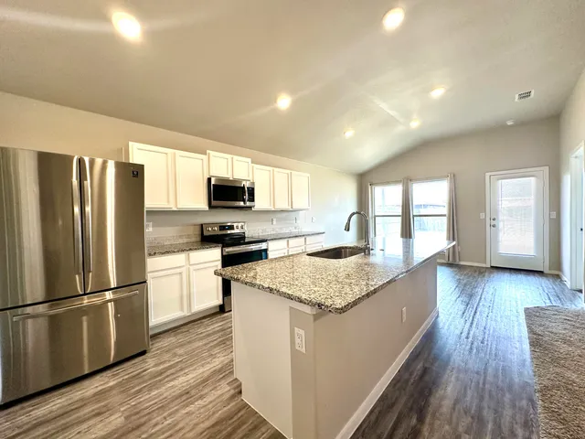 a kitchen with stainless steel appliances granite countertop a refrigerator a stove top oven a sink dishwasher and wooden floor