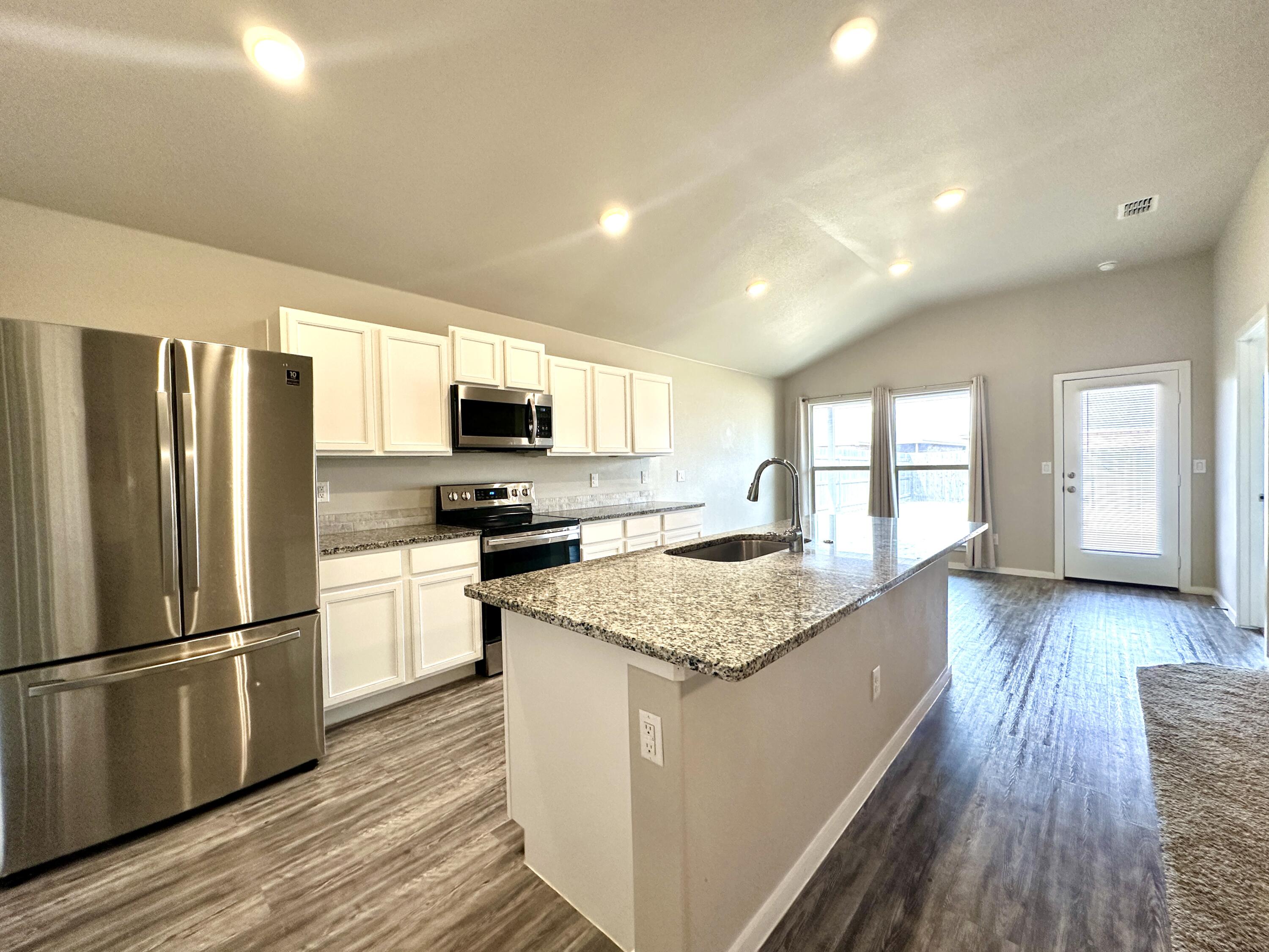7526 31st Place Lubbock, TX 79407 - Photo 5 of 14 a kitchen with stainless steel appliances granite countertop a refrigerator a stove top oven a sink dishwasher and wooden floor