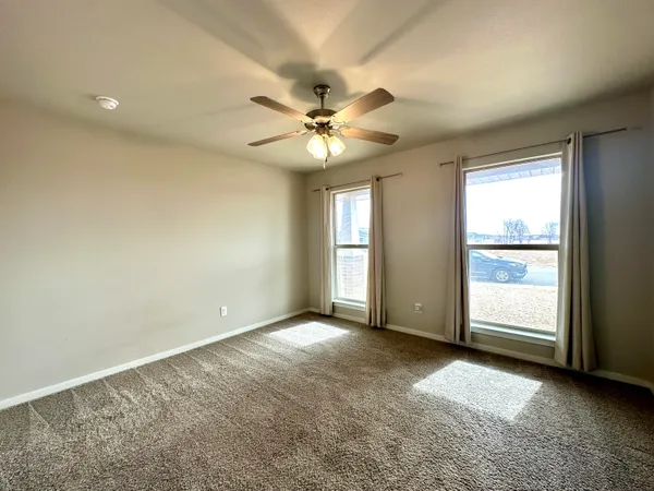 an empty room with chandelier fan and windows