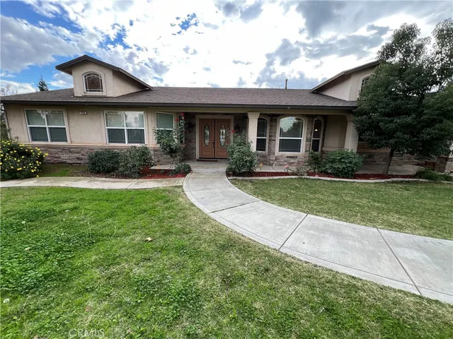 a view of a brick house with a big yard plants and large trees