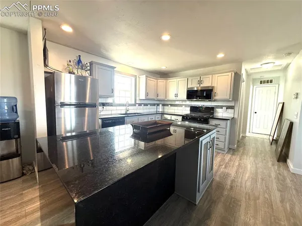 a kitchen with stainless steel appliances granite countertop a refrigerator a stove top oven a sink dishwasher and wooden cabinets with wooden floor