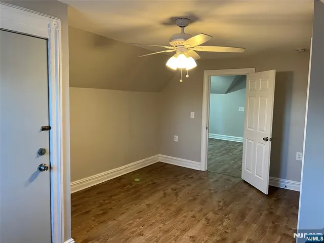 an empty room with a chandelier fan and wooden floor