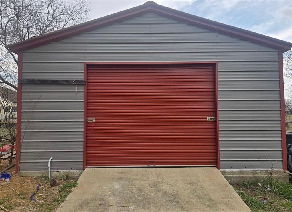4378 Old Fort Worth Road Midlothian, TX 76065 - Photo 6 of 6 This property features a structure with gray corrugated metal siding, accented by red trim on the roofline and around the large red roll-up door