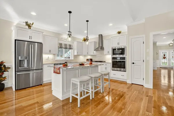 a kitchen with stainless steel appliances kitchen island granite countertop a refrigerator a stove and white cabinets with wooden floor