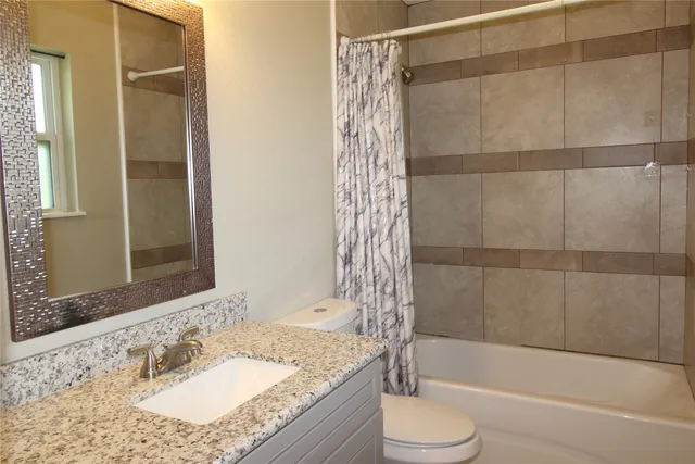 a bathroom with a granite countertop bathtub shower sink vanity and toilet