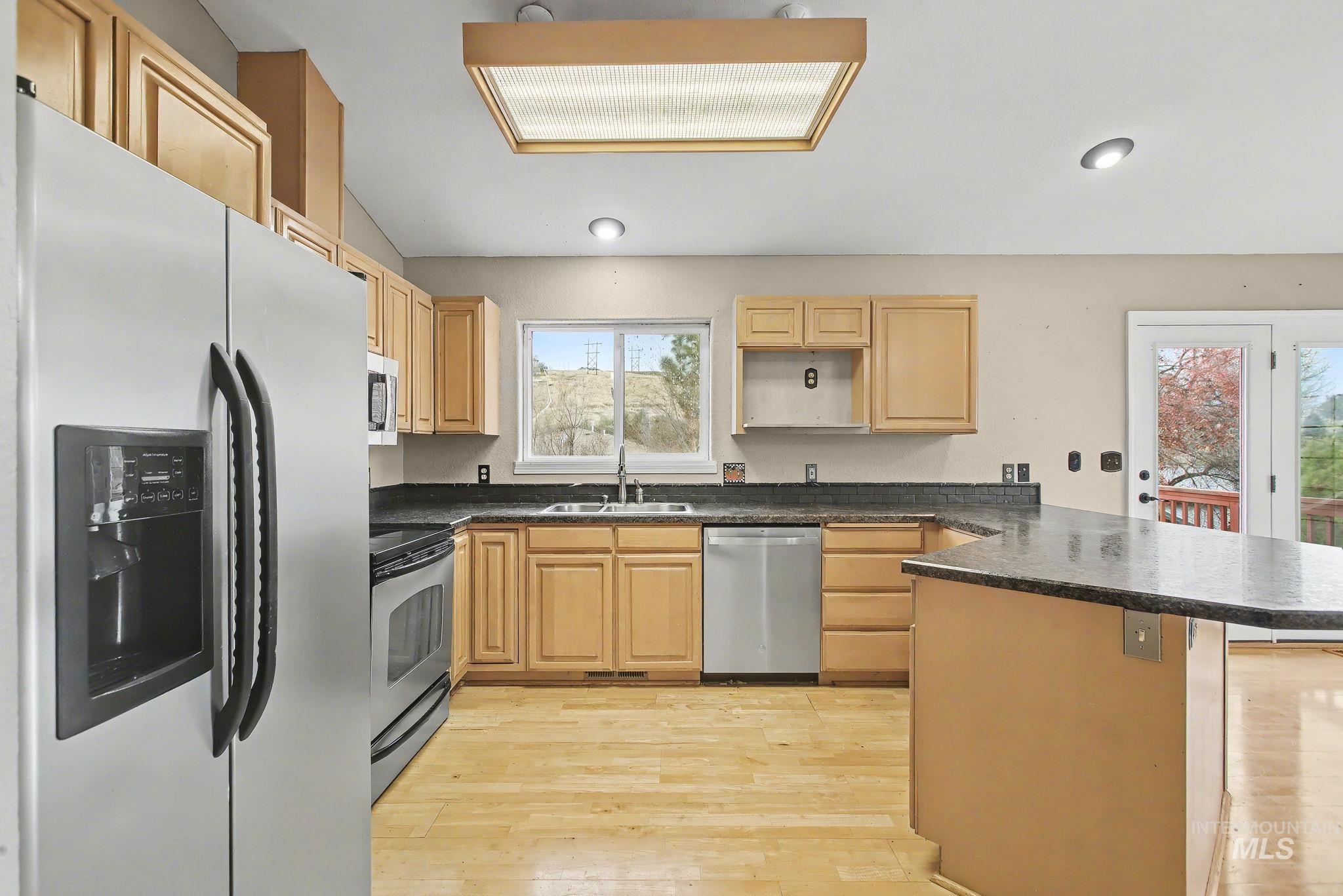 2242 Chukar Lane Clarkston, WA 99403 - Photo 13 of 41 Kitchen with stainless steel appliances, light wood-type flooring, a peninsula, light brown cabinets, and dark stone countertops