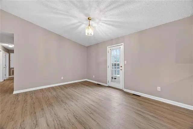 an empty room with wooden floor chandelier fan and windows