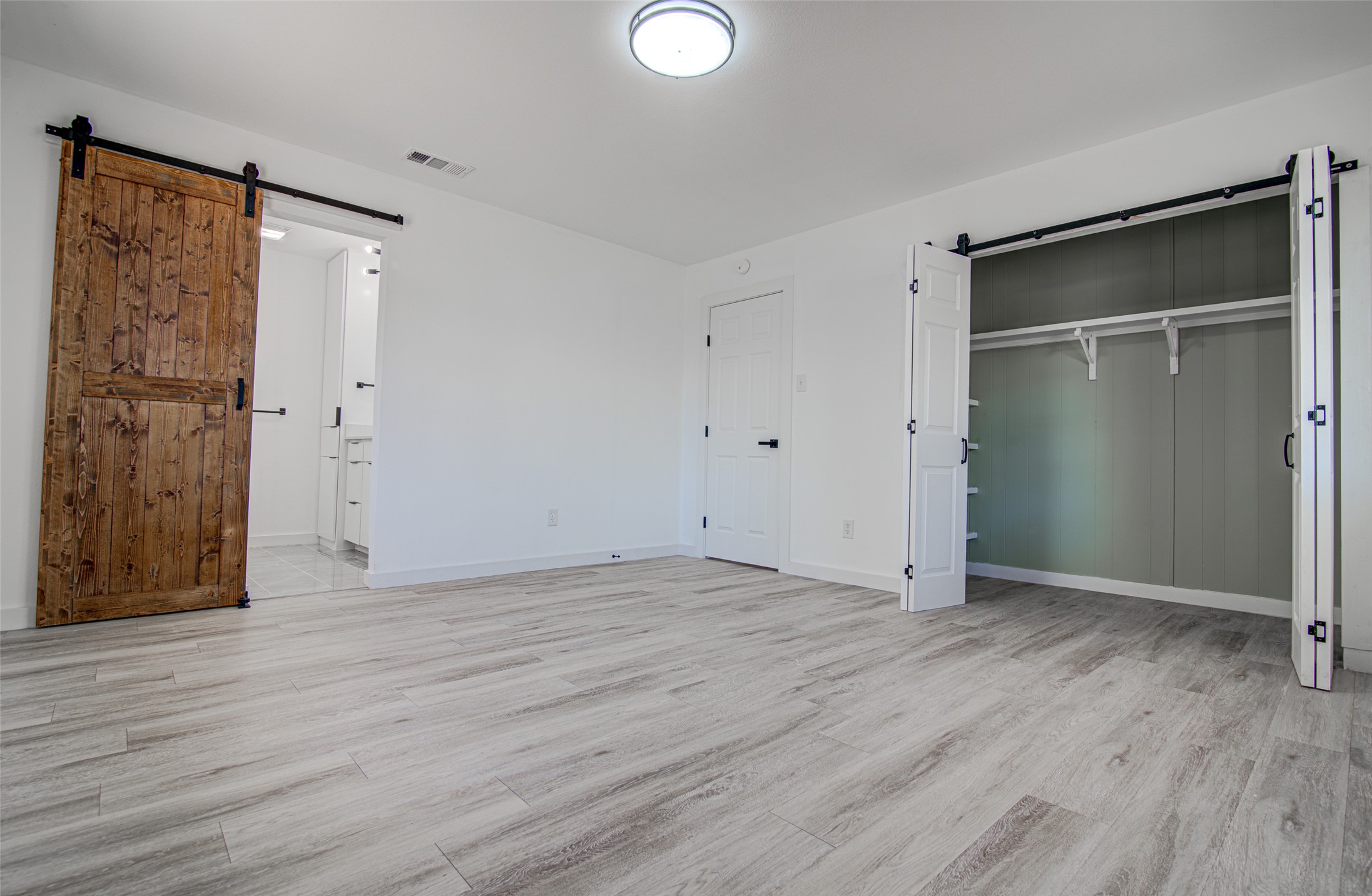 207 Haley Road Johnson City, TX 78636 - Photo 14 of 31 Natural wood barn doors lead to a well-appointed primary bathroom, complemented by a spacious closet.