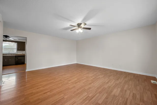 an empty room with wooden floor chandelier fan and windows