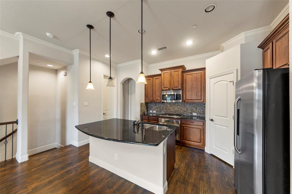 7929 Maddox Road Plano, TX 75024 - Photo 4 of 26 Kitchen with wood finish cabinets, stainless steel appliances, dark stone countertops, a kitchen island with sink, and crown molding