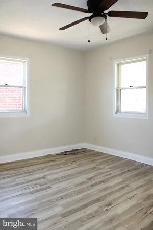 an empty room with wooden floor fan and windows