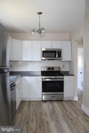 a kitchen with granite countertop a stove top oven a sink dishwasher a refrigerator and white cabinets
