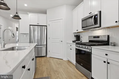 a kitchen with stainless steel appliances white cabinets a sink a stove a refrigerator and island with wooden floor
