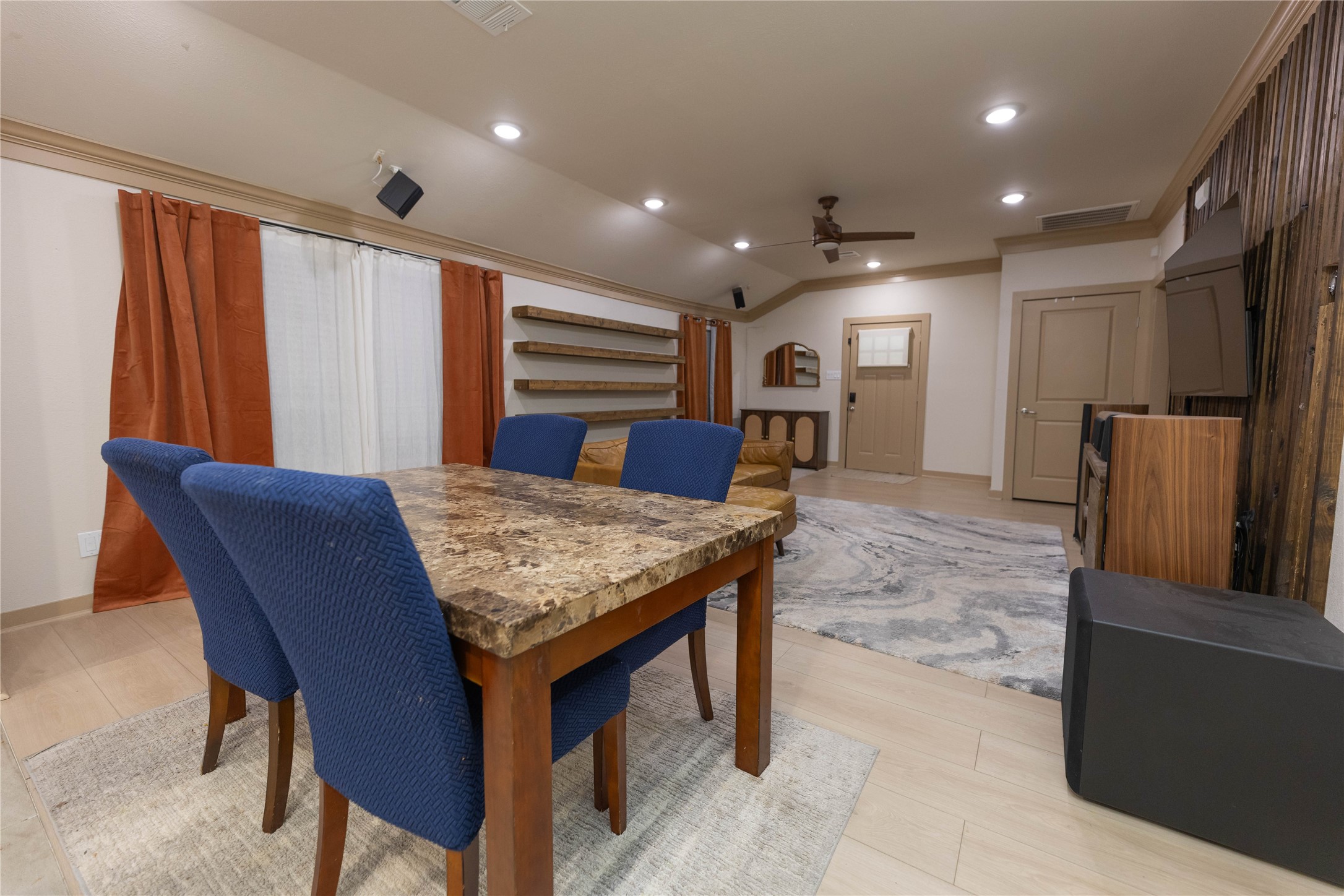 8007 Capitol Street Houston, TX 77012 - Photo 14 of 25 This room features an open layout with a dining area, highlighted by a marble-top table and blue chairs. It has modern lighting, wood accents, and a seating area with a wall-mounted TV for entertainment. The space is versatile, ideal for both dining and relaxation.
