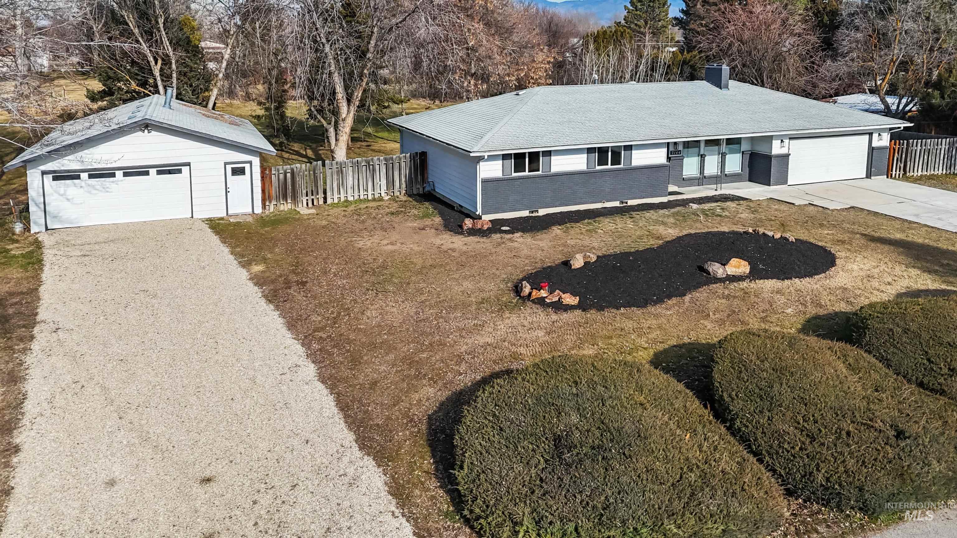 Single story home with driveway, an outdoor structure, a chimney, roof with shingles, and view of wooded area