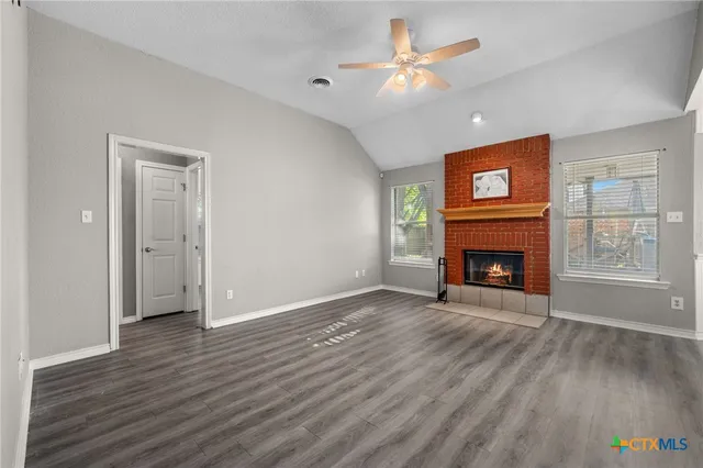 an empty room with windows a fireplace a ceiling fan and wooden floor