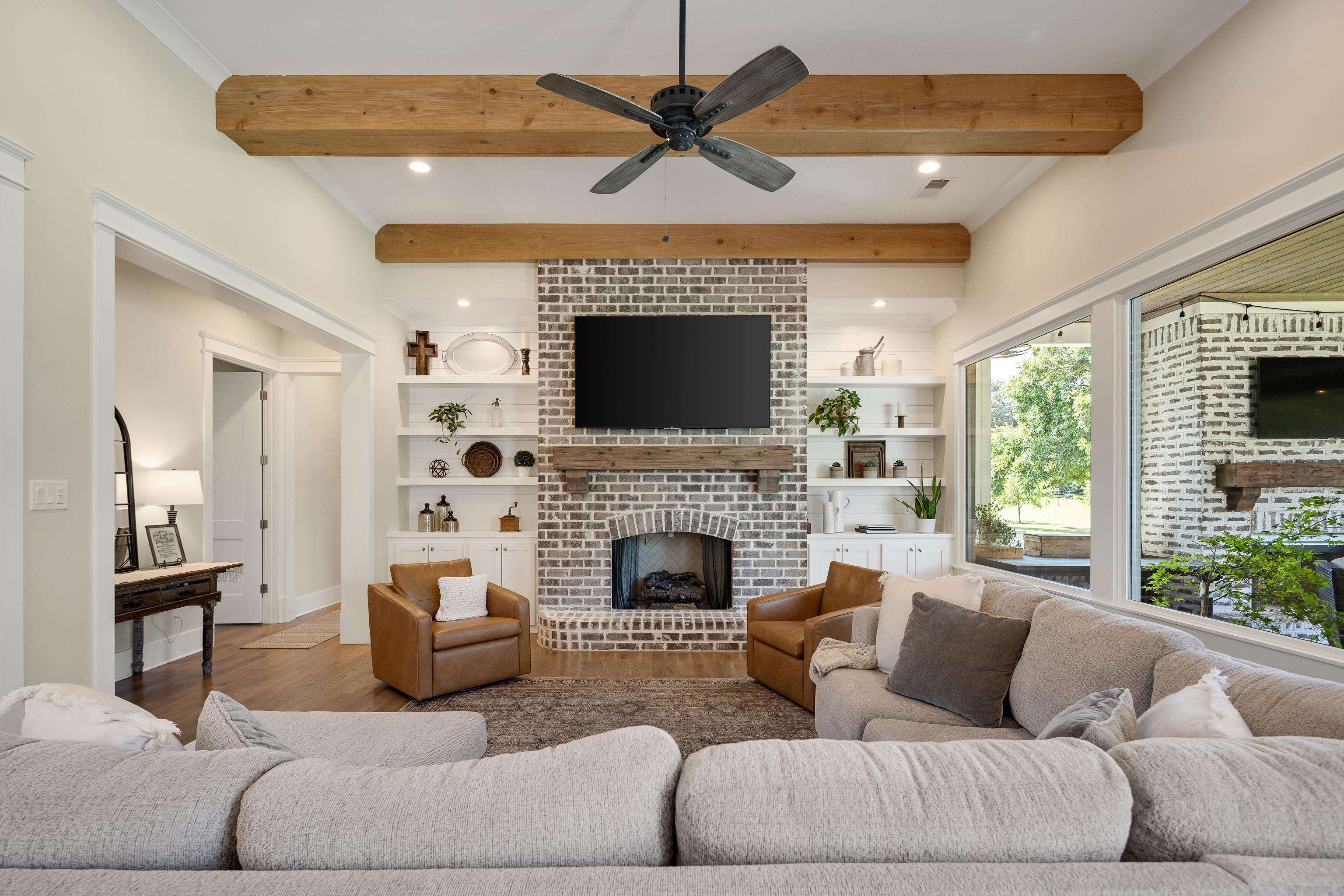 805 Shady Grove Road Williston, TN 38076 - Photo 8 of 40 Exposed wood ceiling beams, brick-clad fireplace with wood mantel, built-in shelving, expansive windows, and wood-finish flooring