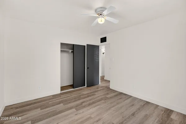 a view of an empty room with wooden floor and a ceiling fan