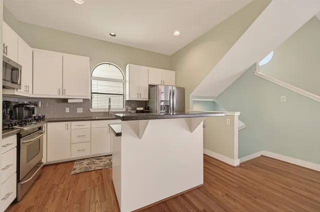 a kitchen with kitchen island granite countertop a stove top oven a sink and white cabinets with wooden floor