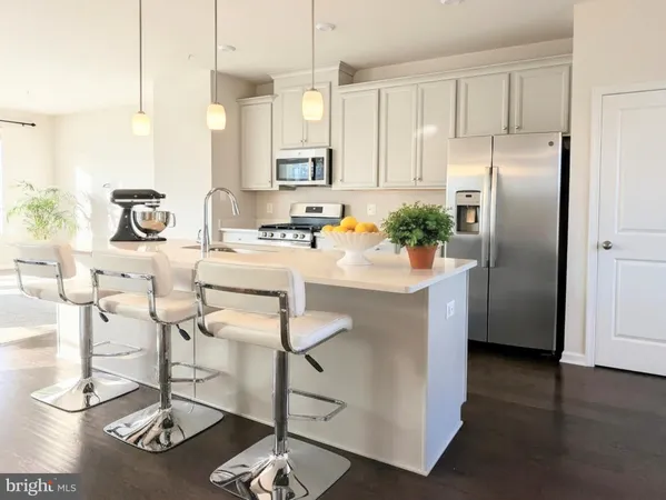 a kitchen with stainless steel appliances kitchen island granite countertop a refrigerator a stove and white cabinets with wooden floor